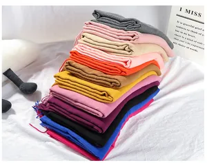 Stack of colorful solid cashmere-like scarves with tassel details in a cozy setting.