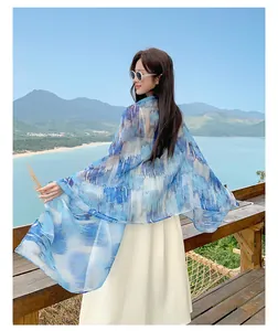 Woman wearing a blue printed sunscreen shawl overlooking a scenic ocean beach
