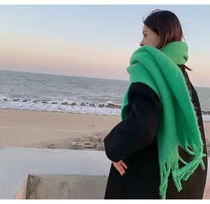 Stylish woman wearing a bright green mohair-like winter scarf on a beach at sunset
