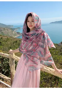 Model wearing a pink printed Bali yarn scarf as a sun protection shawl by the coast.