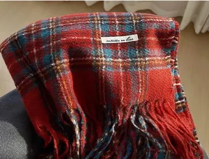 Detailed close-up of a cozy red plaid cashmere scarf with soft tassels and label.
