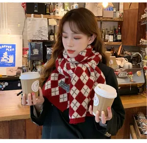 Red and white argyle knit scarf worn by a model in a cozy autumn cafe setting