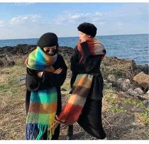 Detailed look of two models wearing thick plaid mohair scarves with tassels at the beach.