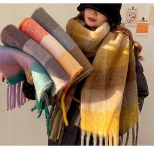 Variety of colorful thick mohair plaid scarves with tassels held by a model in winter
