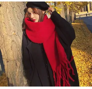 Model wearing a vibrant thick red wool scarf with tassels in a scenic autumn outdoor setting
