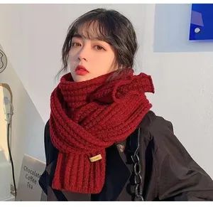 Close-up of a chunky dark red knitted scarf with a handmade label on an Asian model.