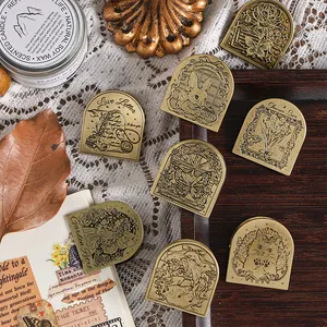 Vintage brass paper clips with engraved retro designs on a wooden tray