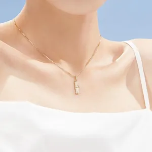 Vue détaillée d'un collier doré avec pendentif en bambou sur le cou d'une femme.