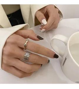 Close-up view of a hand wearing minimalist silver smiley and wave textured rings near a cup