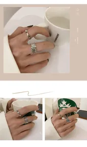 Close-up detail of minimalist silver smiley face and wave pattern rings on hand holding mug