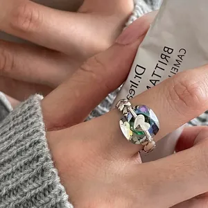 Close-up of geometric iridescent crystal ring with silver heart detail on finger.