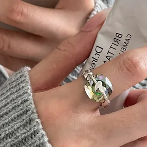 Close-up detail of a silver heart ring with a large green geometric cushion-cut gemstone.