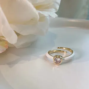 Macro view of a delicate gold heart ring featuring pink crystal and white enamel details