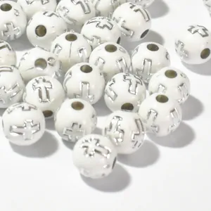 Macro detail of 8mm white acrylic beads featuring silver engraved cross patterns for DIY crafts