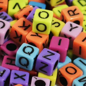 Macro view of colorful 6mm acrylic cube beads featuring black printed alphabet letters