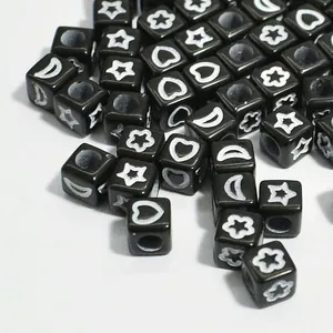Macro view of 6mm black acrylic cube beads with white star, moon, and heart patterns.