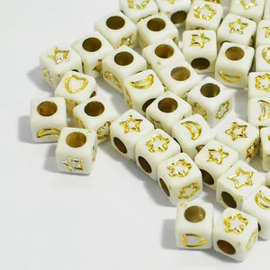Close-up of 6mm white acrylic cube beads with gold star and moon patterns for DIY jewelry.