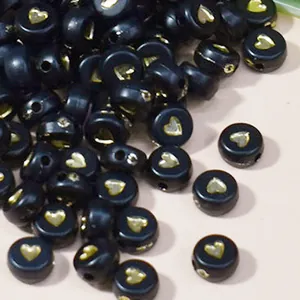 Dettaglio ravvicinato di perline acriliche nere da 7mm con cuori dorati per il fai da te.