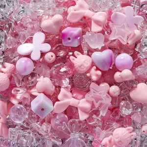 Close-up of mixed pink and clear acrylic beads in heart and bow shapes for DIY crafts.