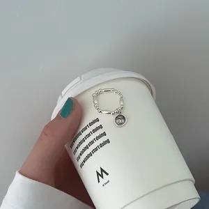 Nahaufnahme eines minimalistischen silbernen Perlenrings mit Smiley auf einem Becher