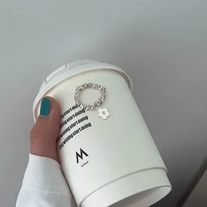 Nahaufnahme eines elastischen Silberperlenrings mit weißem Blumenanhänger auf Becher