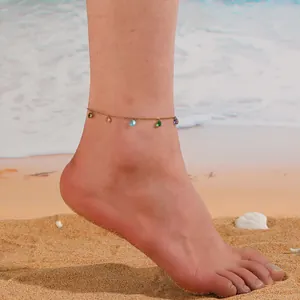 Gros plan d'une chevillère à pierres colorées sur le sable avec des breloques en zircone