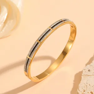 Macro shot of gold-plated stainless steel bangle with black enamel and rows of crystals.