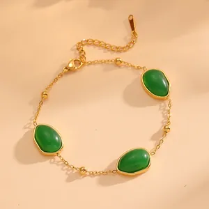 Gros plan d'un bracelet en acier doré avec des pierres vertes ovales et perles.
