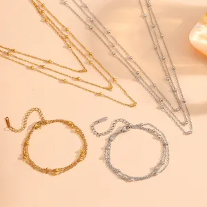 Detail view of layered bead chain necklaces and bracelets in gold and silver steel.