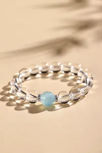Detailopname van een heldere kwarts kralenarmband met een blauwe aquamarijn kraal.