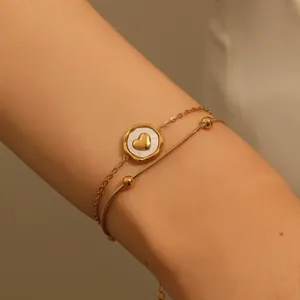 Detailed view of an elegant double-layered gold heart pendant bracelet on a wrist.