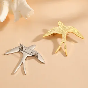 Detailed view of gold and silver swallow-shaped titanium steel brooches on beige backdrop.