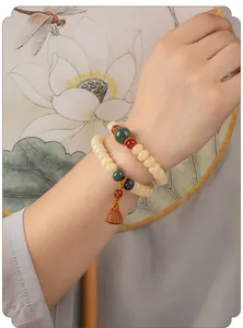 Detailopname van een dubbelstrengs crèmekleurige bodhi-wortelarmband met lotushanger