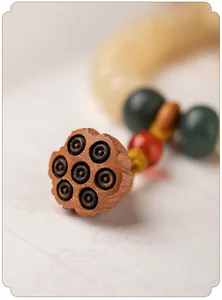 Detailopname van een crèmegele Bodhi wortel armband met een gesneden houten lotus hanger