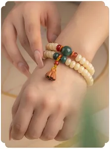 Detail van een dubbellaagse Bodhi-wortelarmband met lotuspeul-bedeltje om de pols.