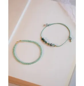 Vista detallada de pulseras de ágata musgosa y cuentas de oro de 14k en un libro.