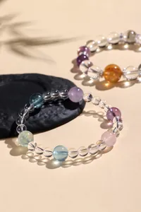 Detailansicht von Armbändern aus klarem Quarz und bunten Edelsteinen auf strukturiertem Stein