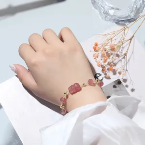 Verfijnde aardbeienkwarts armband met gouden Pixiu-bedel om de pols van een vrouw.