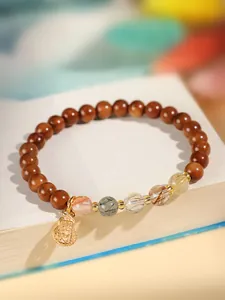 Nahaufnahme des Armbands aus Naturholz und Phantomschmuck mit goldenem Flaschenkürbis-Anhänger