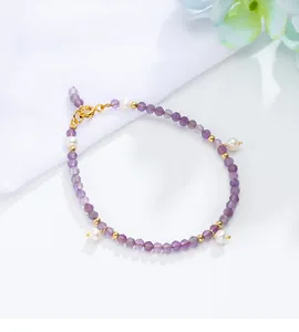 Detail van een armband van paarse amethist en witte parels met gouden accenten