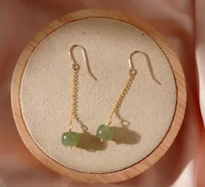 Gros plan d'élégantes boucles d'oreilles en chaîne dorée avec perles de jade.