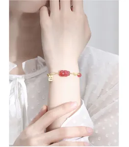 Detailweergave van een aardbeienkwarts armband met gouden gelukshanger om de pols.