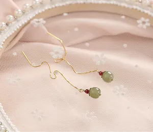 Détail d'élégantes boucles d'oreilles dorées avec perles de jade vert et pierres rouges.