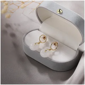 Élégantes boucles d'oreilles en jade blanc naturel dans un écrin en velours gris.