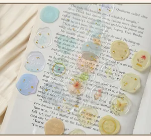 Dettaglio di vari adesivi per sigilli in cera floreali pastello e trasparenti su un libro.