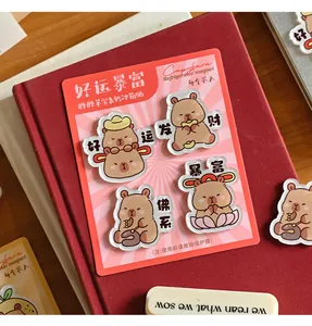 Détail de quatre jolis aimants de frigo Capybara en acrylique posés sur un livre rouge
