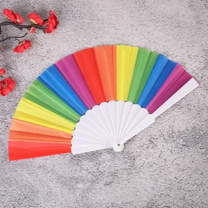 Vibrante abanico plegable arcoíris con varillas de plástico blanco sobre fondo gris.