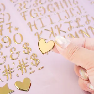 Close-up of a gold 3D puffy heart sticker being held to show its metallic texture and depth.