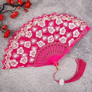 Details of vibrant pink Chinese vintage folding fan with white floral embroidery and tassel.