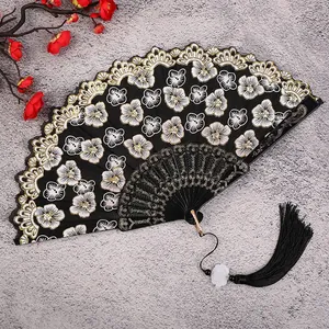 Detailed shot of traditional Chinese folding fan with black gold floral embroidery and tassel.